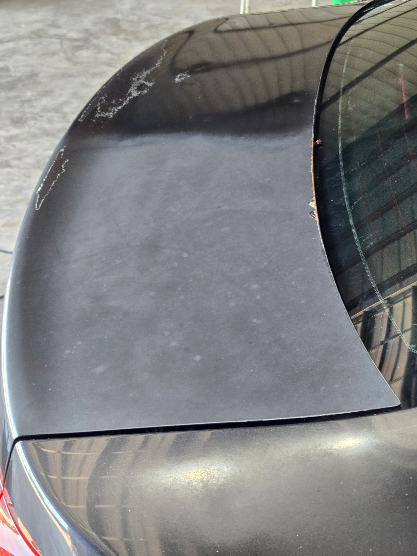 Black sedan trunk and spoiler paint close-up before paint correction